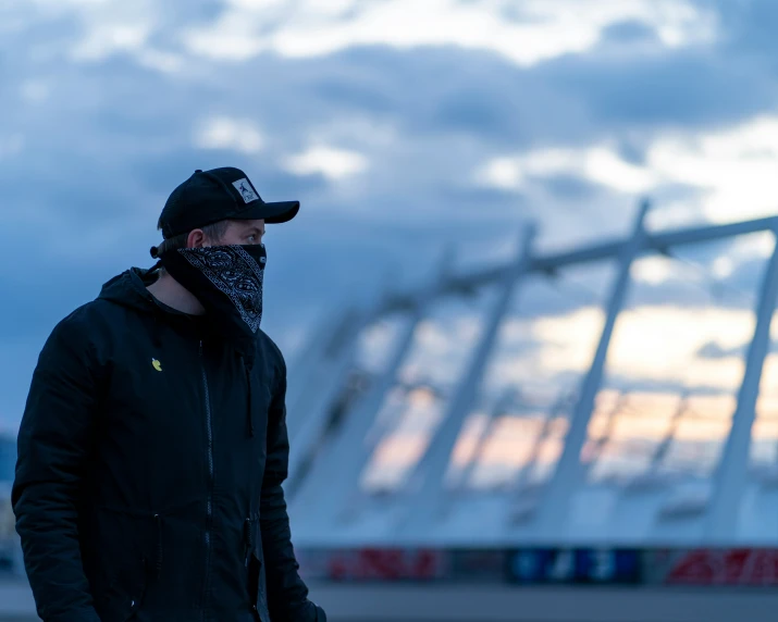 man in black jacket and bandana standing in front of large metal structure