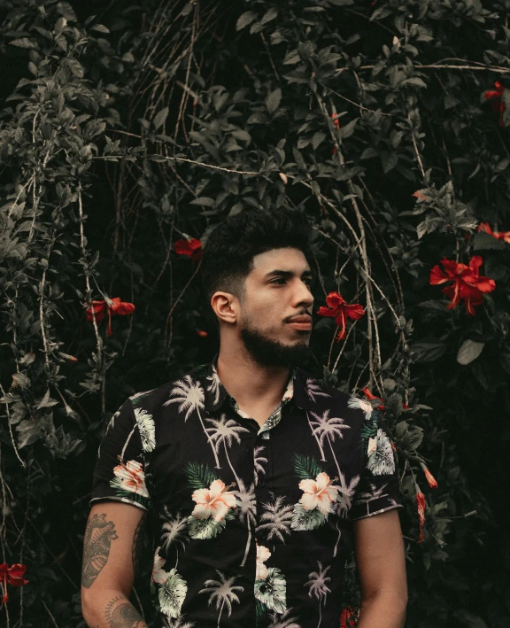 a man with black hair and tattoos standing in front of flower covered tree