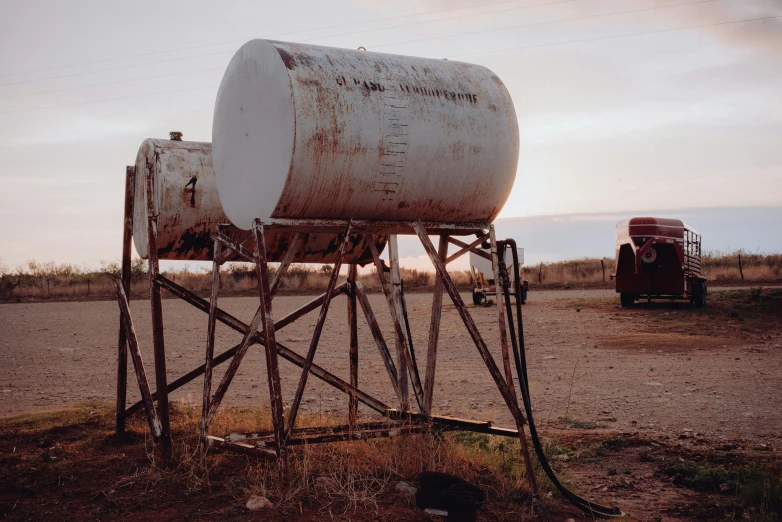 two old trucks sit parked near a large tank