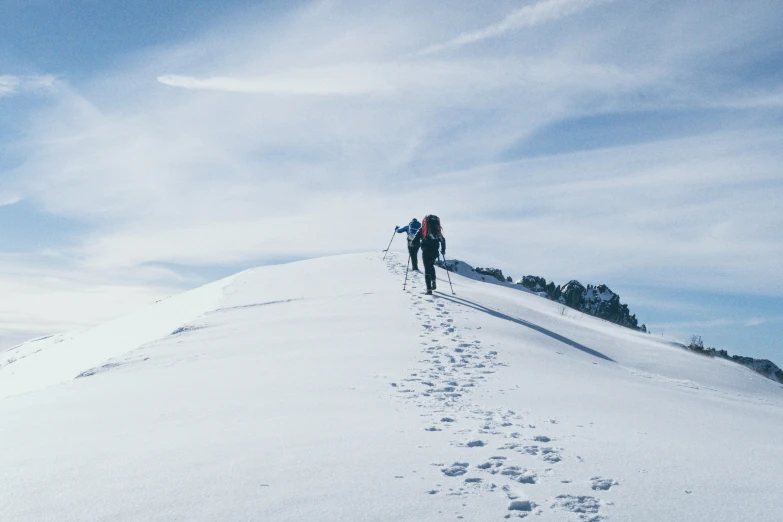 a couple of people walking up the side of a snow covered hill