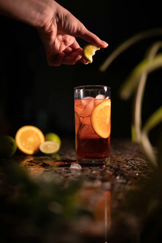 a hand is reaching for an orange near a glass