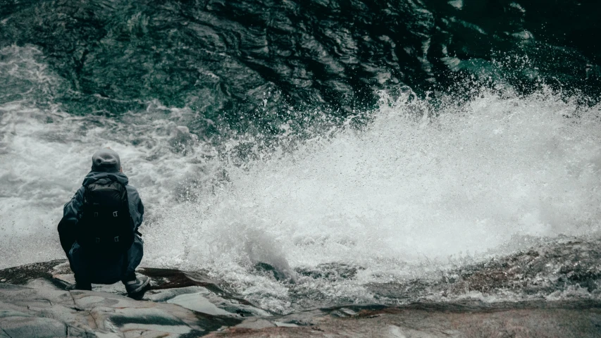 a man stands on rocks and looks at the rough waters