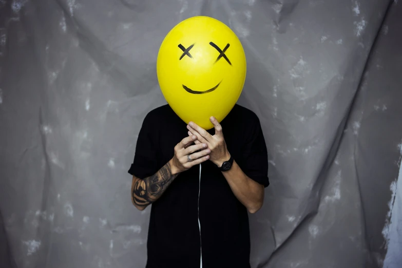 a man with a black shirt on holds a balloon in the shape of a smiling face