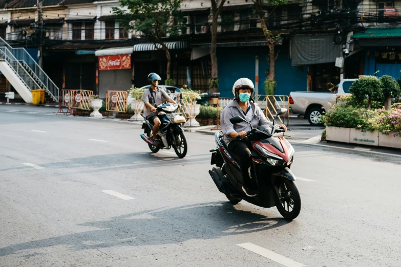 two men wearing masks ride motorcycles down a city street