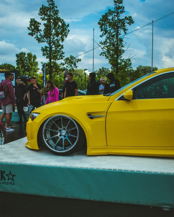 a yellow bmw car with people looking at it