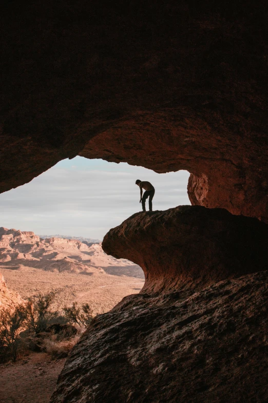 man standing in the hole of an oddly shaped formation of rock