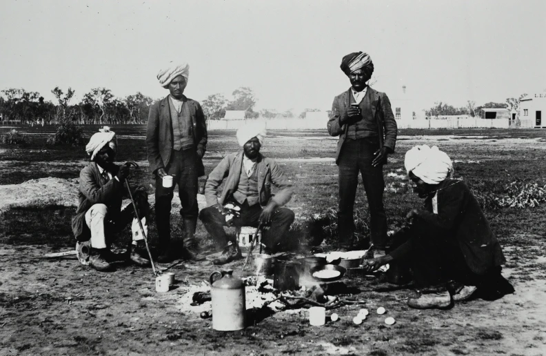 four men sitting next to each other near pots and pans