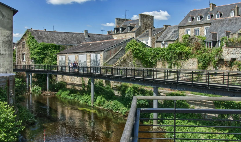 the view of the street bridge through the river runs past an old brick building and a row of three story houses