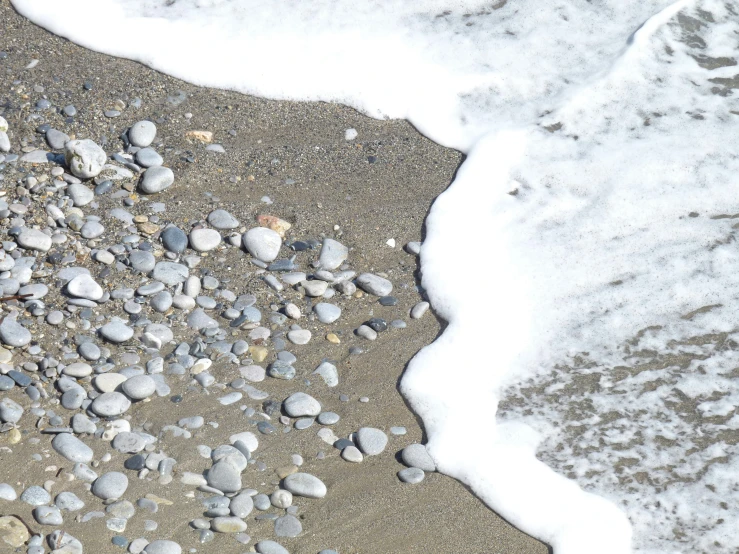 the sand and rocks are in front of the ocean wave