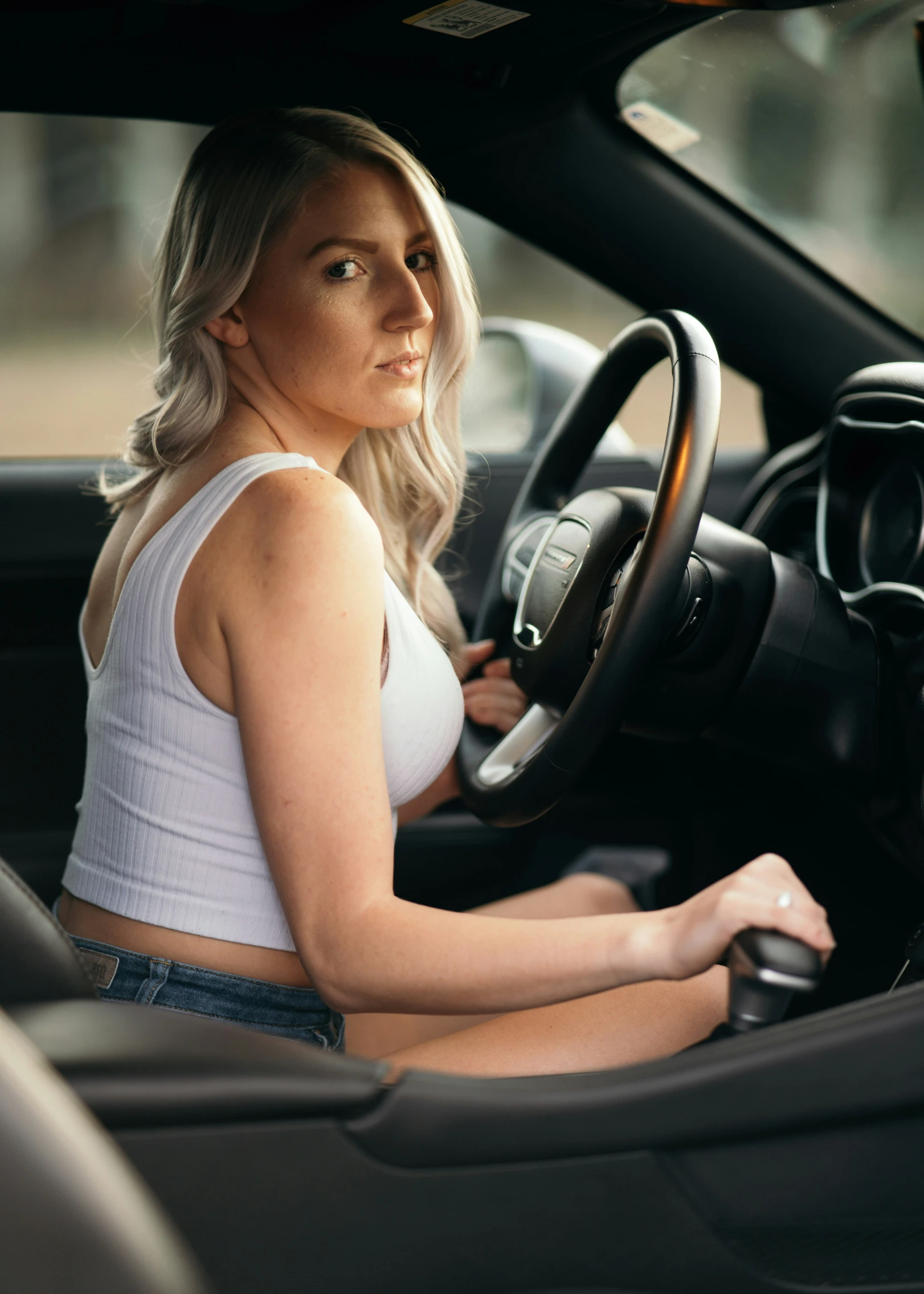 the woman sitting in the driver's seat is holding the steering wheel and wearing jeans