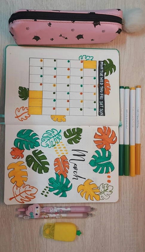 an open planner on a wooden table and some markers