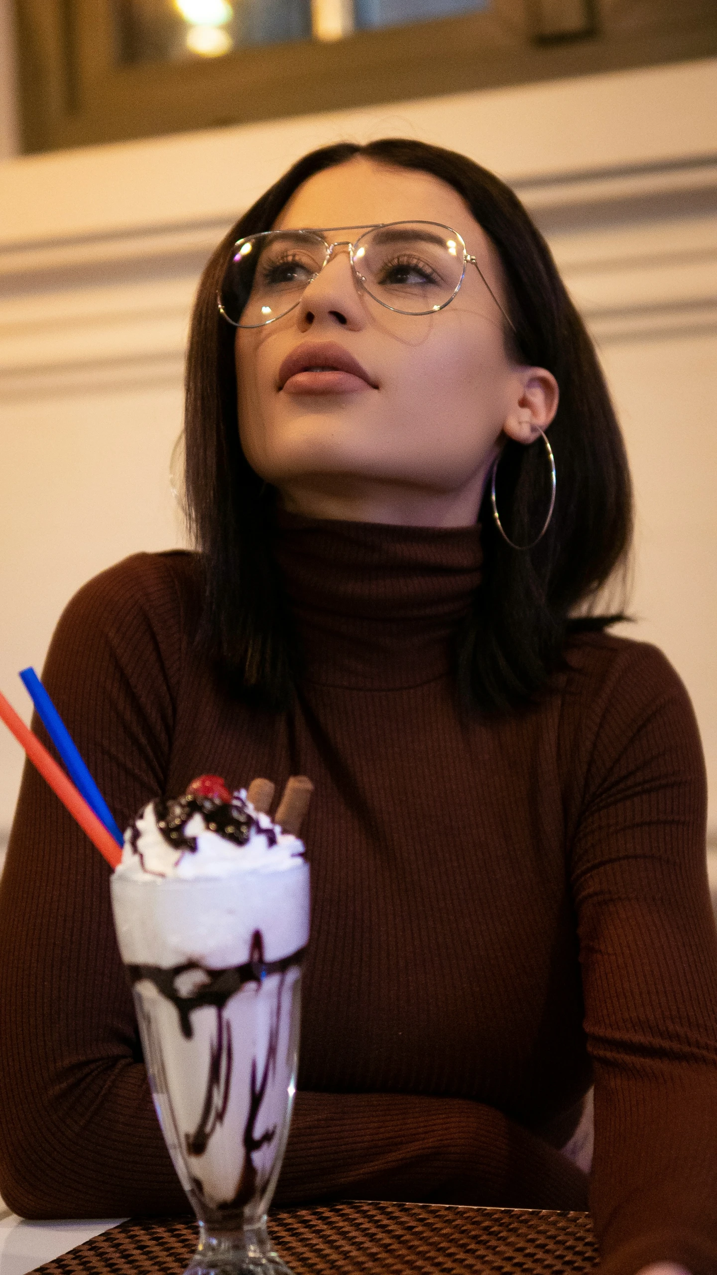 woman wearing glasses sitting at a table with a cup full of milkshake