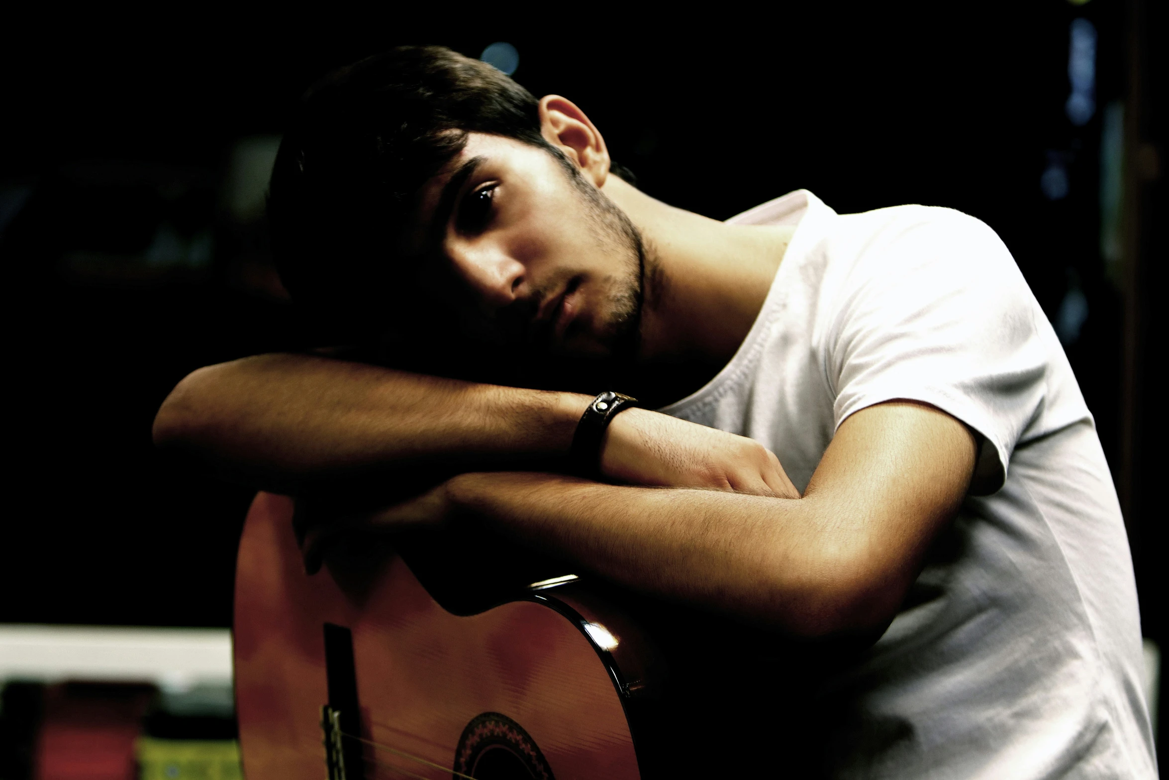 man posing with guitar leaning against his arm and looking off into the distance