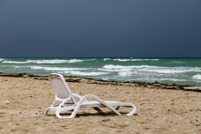 a white lawn chair on a beach facing the ocean