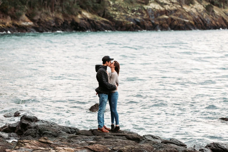 a man and woman kissing on the side of a body of water