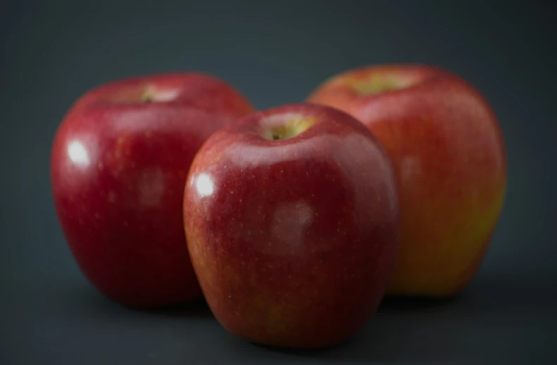 a group of three red apples sitting next to each other