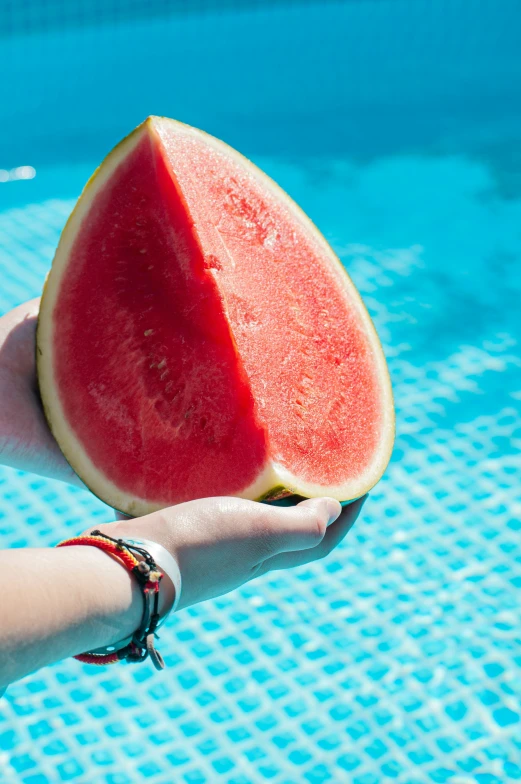 watermelon slice held up by someones hand in the pool