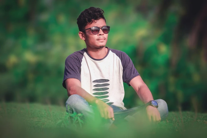 a man wearing glasses and t - shirt while sitting on the ground