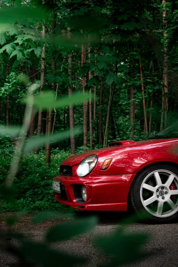 a red car is parked next to a forest