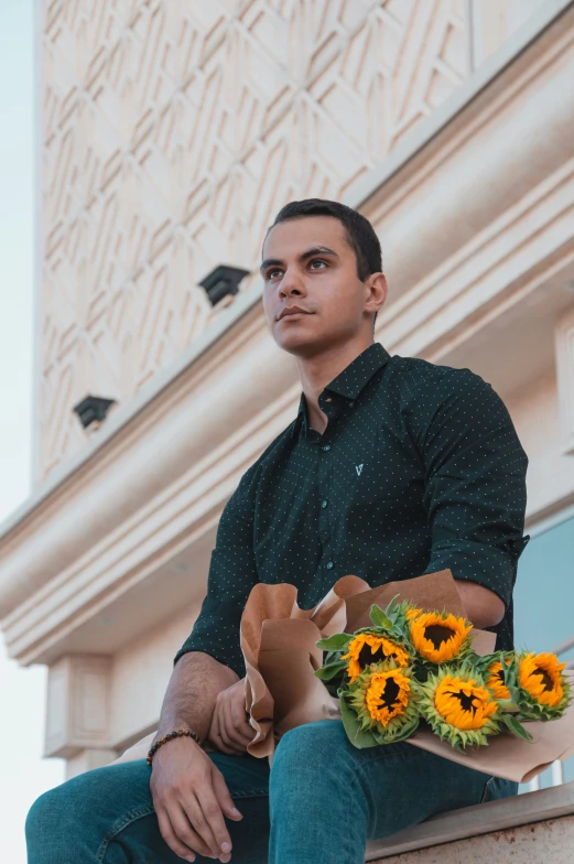 a man sitting on the ledge holding bunches of sunflowers