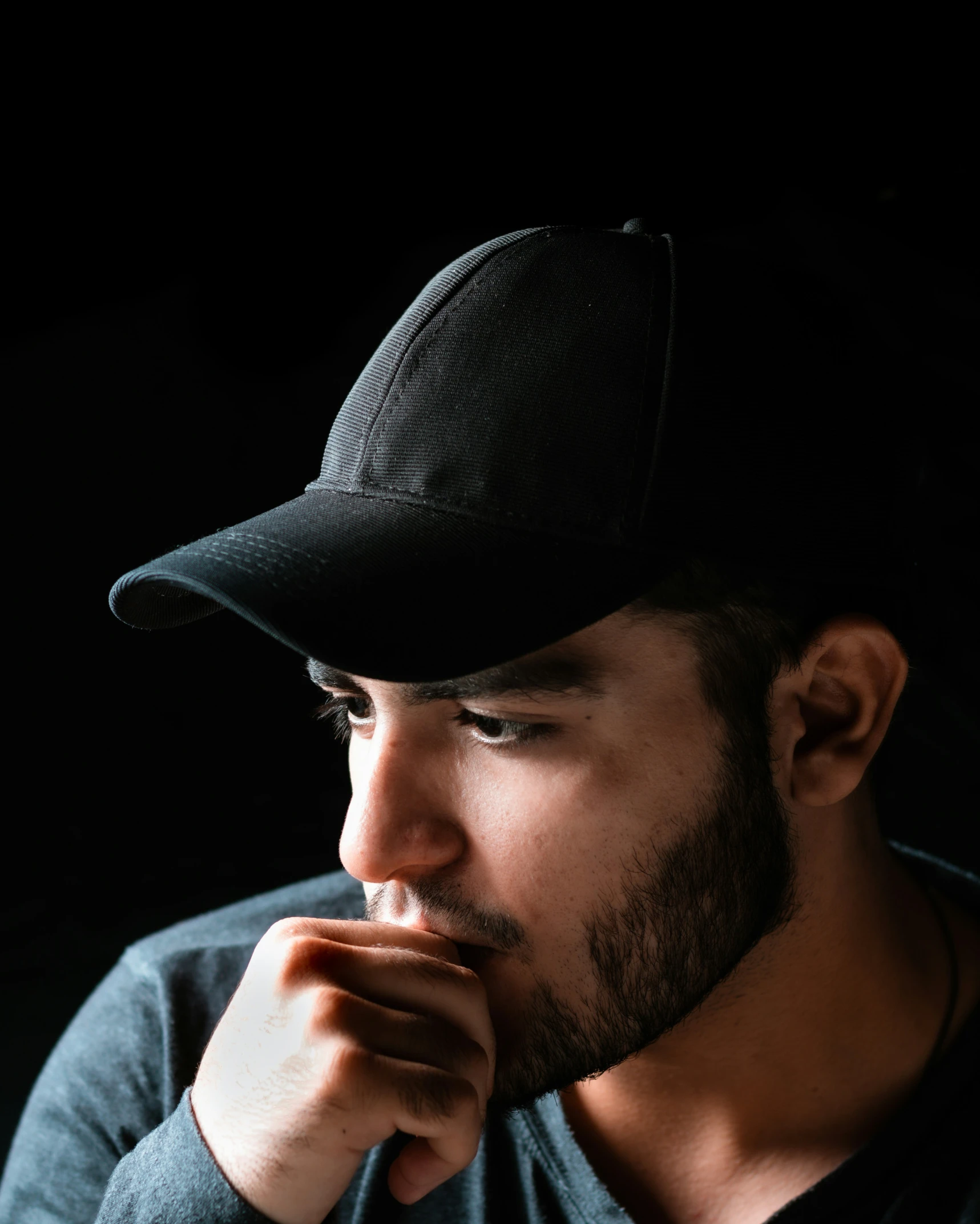 man in hat leaning against black backdrop with hand under chin