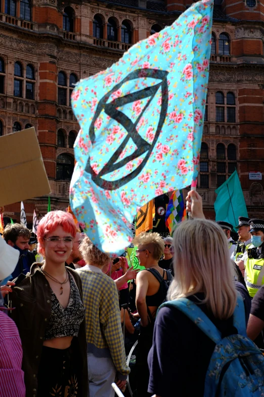 woman wearing pink hair and a colorful scarf is carrying a sign