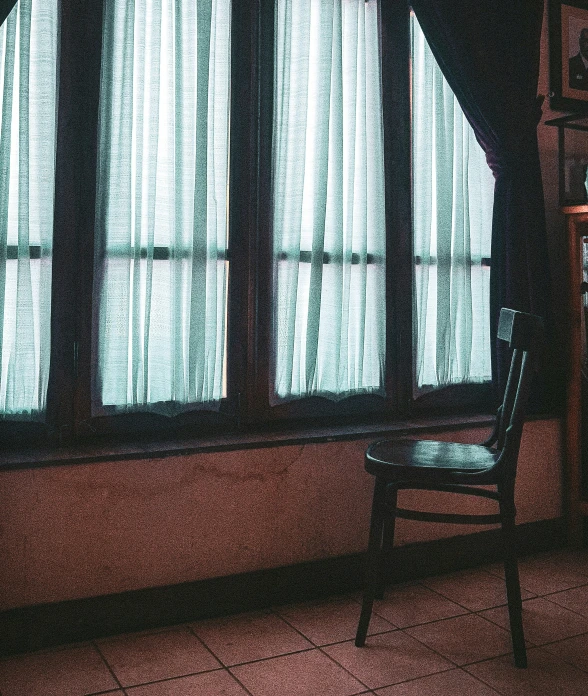 a lonely chair sits in front of the window with curtains