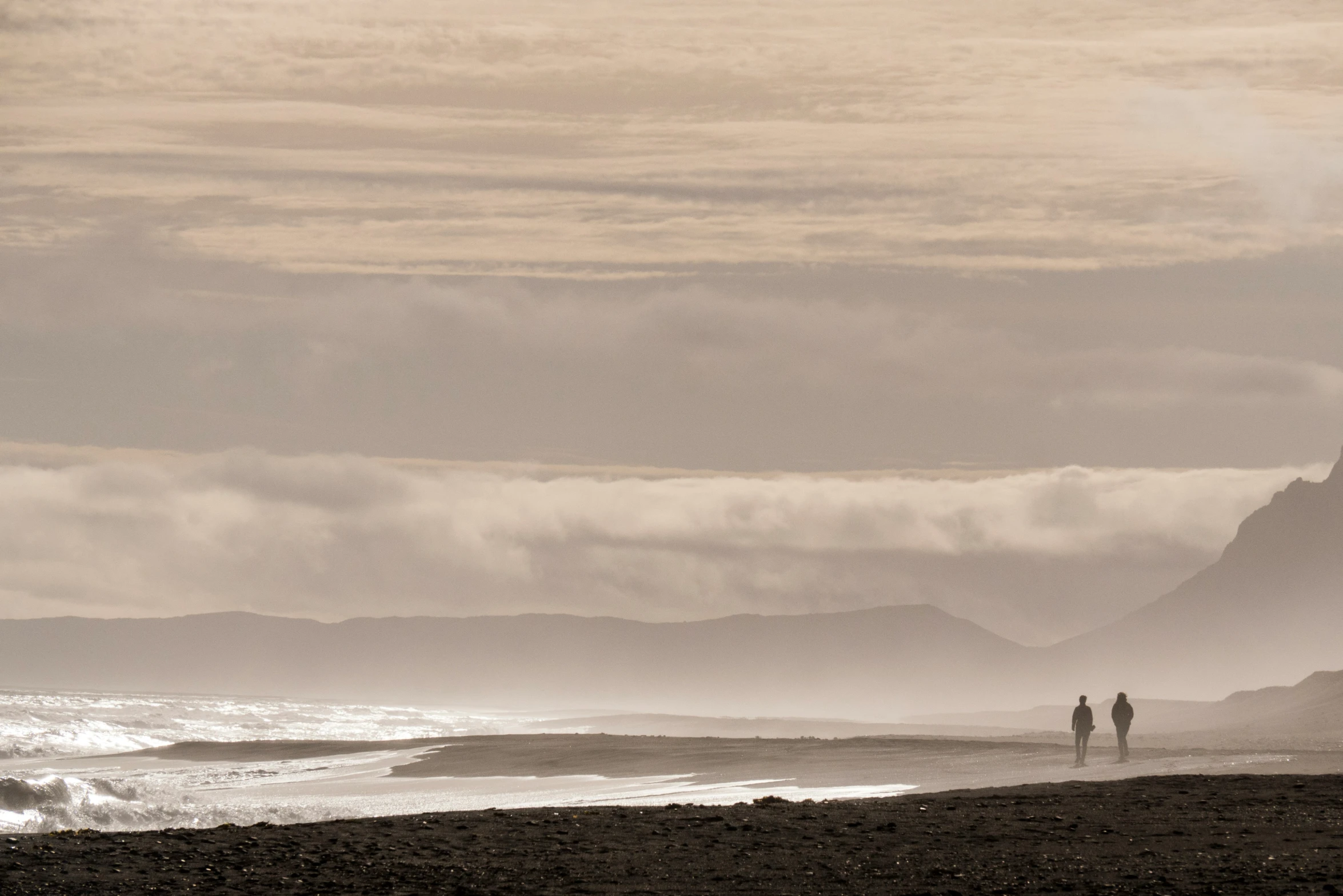 a couple walking on the beach in front of some ocean waves