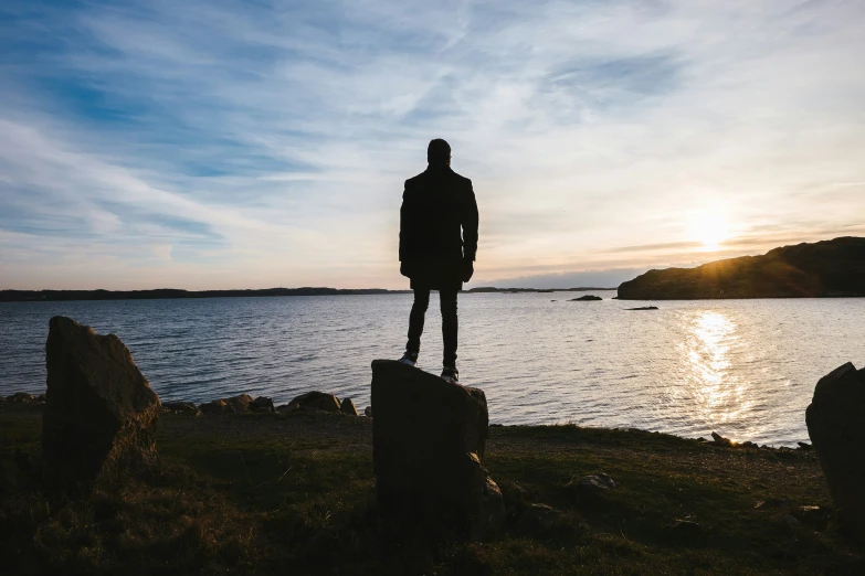 silhouetted person standing on rocks next to a body of water