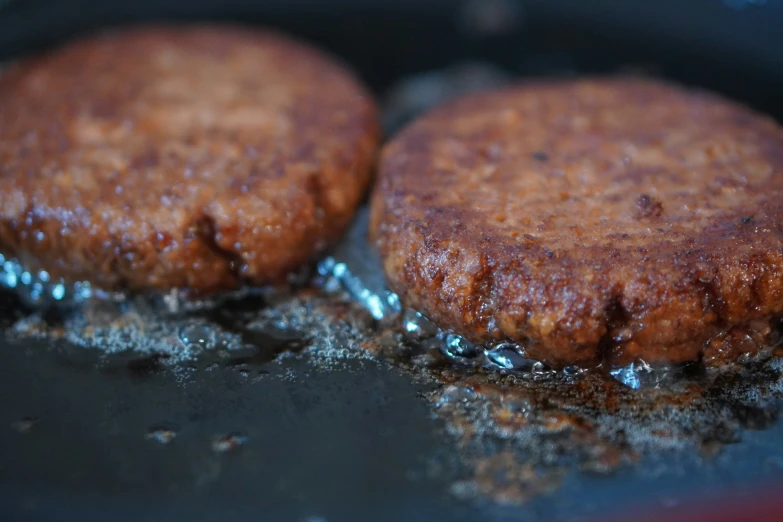 two hamburger patties are being cooked in a black pan