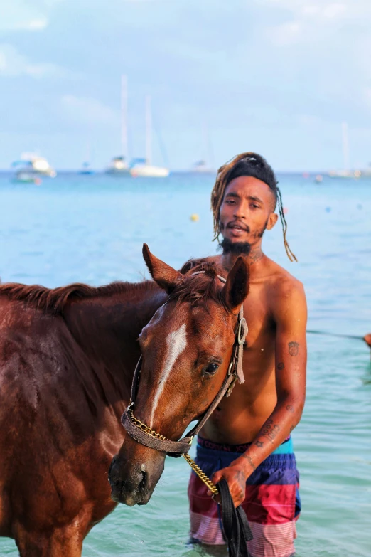 the man stands in the water beside his brown horse