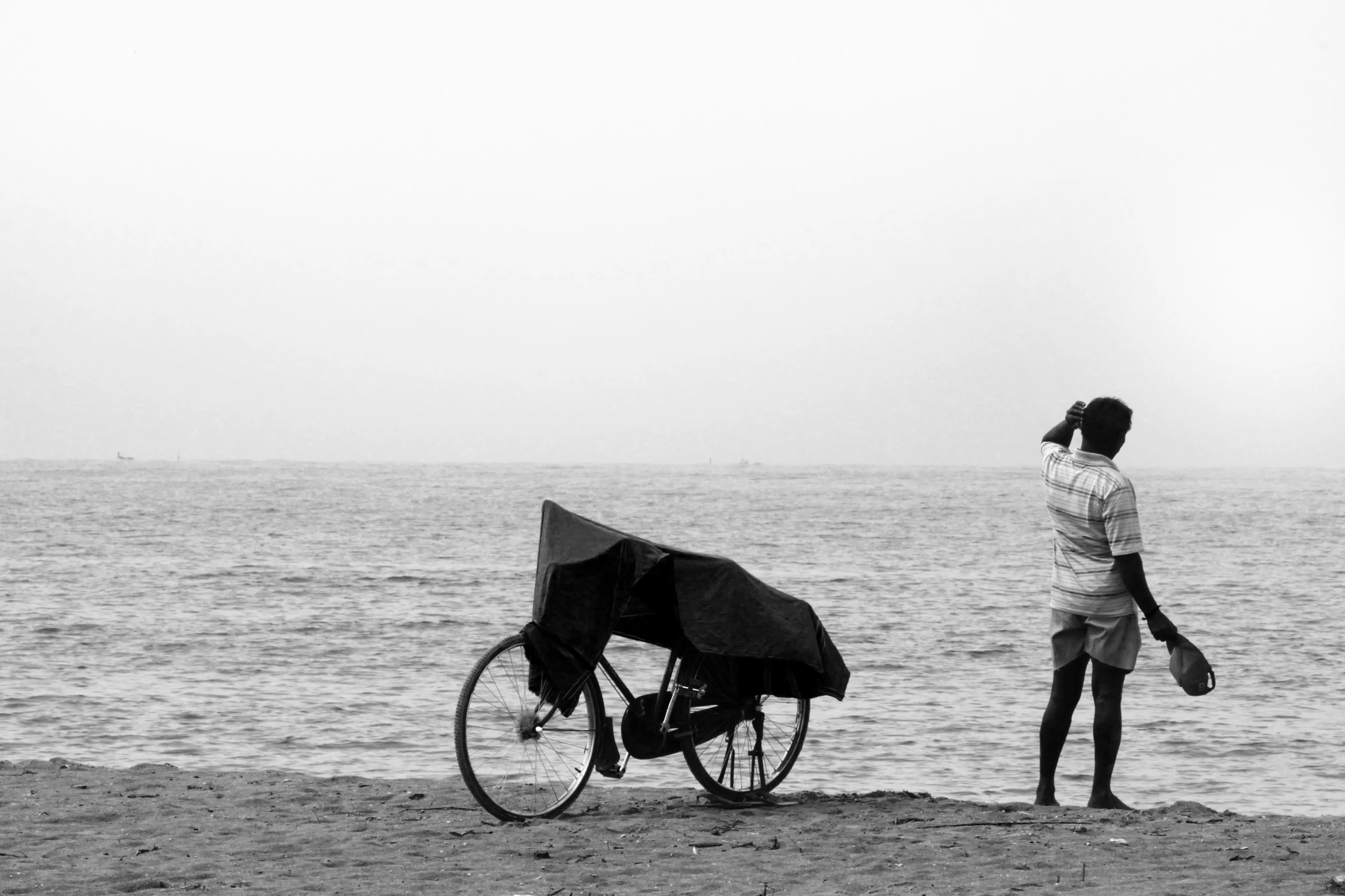 a black and white po of a person standing next to a bike on the beach