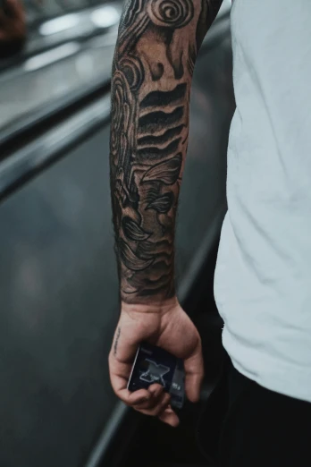 a man with a full sleeve tattoo holds a cell phone in his hand