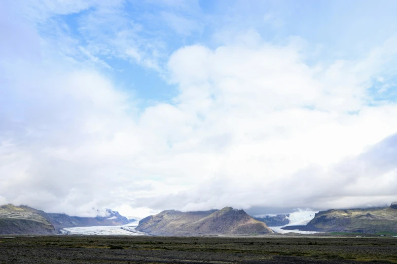 a cloudy sky above some mountains with a stream