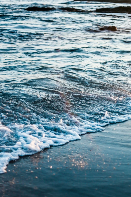 a beach with waves crashing on the sand and people sitting in the ocean