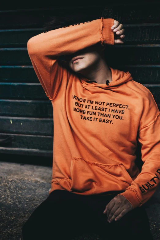 a man sitting in front of a car wearing an orange hoodie