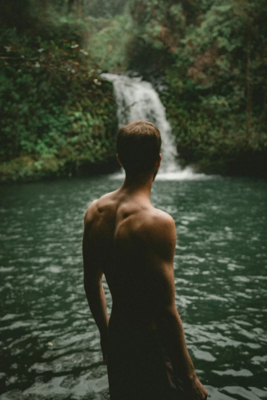 a man looking down at a waterfall in the forest