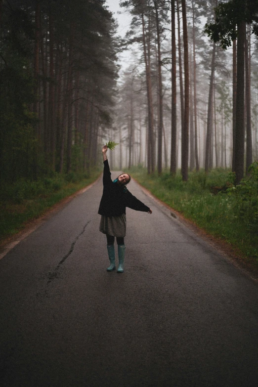 a woman holding an umbrella standing on a road in a forest