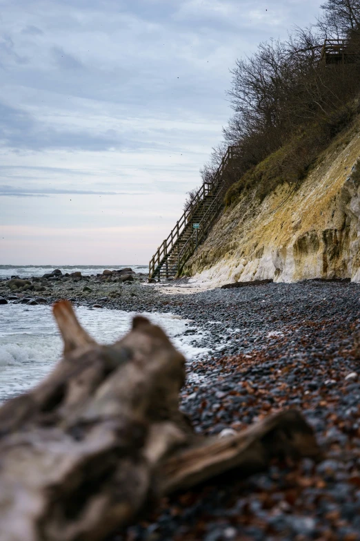 wooden log sitting on beach near cliff and stairs