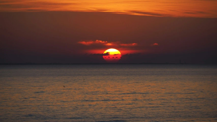 the sun sets over the ocean with large clouds