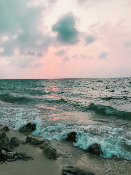 waves crashing onto the beach during sunset with clouds above