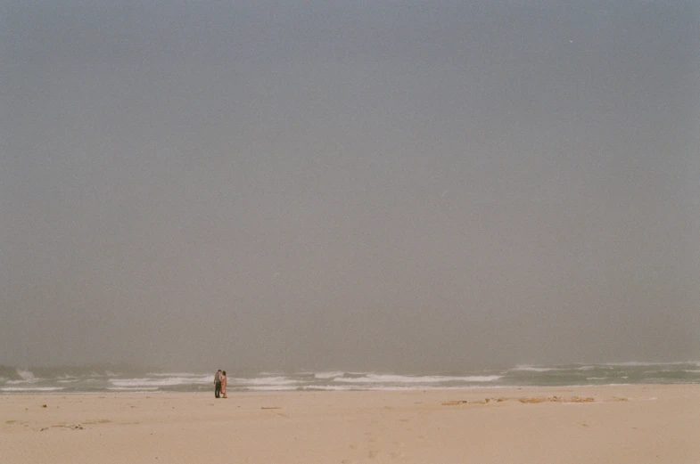 two people are standing in the sand by the water