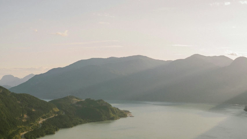 a lone airplane flying over a lake next to some mountains