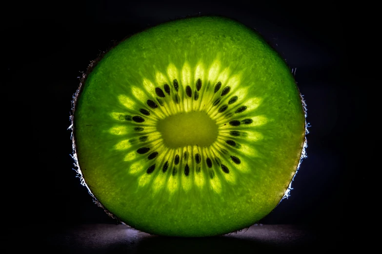 a green kiwi cut in half sitting on top of a black surface