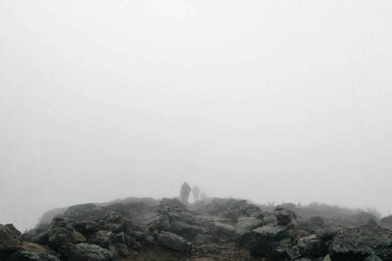 two people standing on top of a large hill in the fog