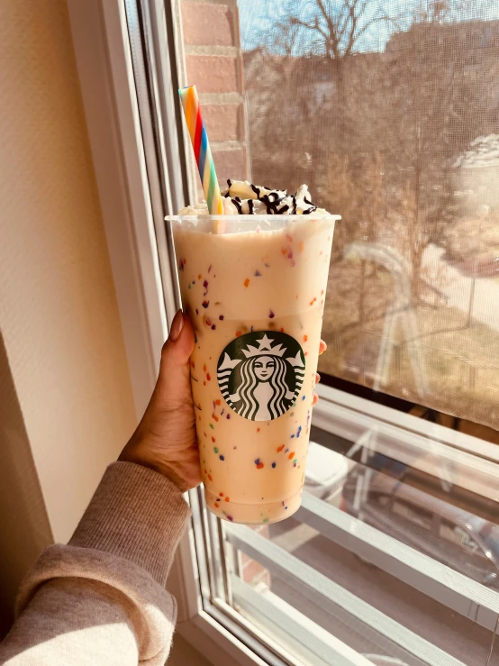 a starbucks drink is held up in a cup in front of a window