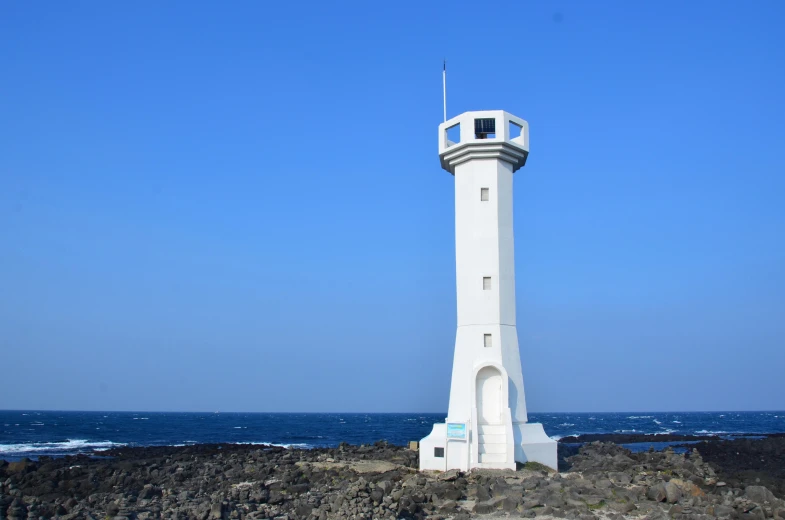 a tall white tower on a rock beach