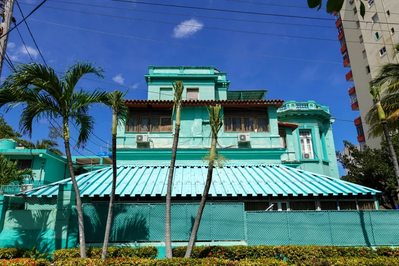 a teal blue building with a blue sky and palm trees
