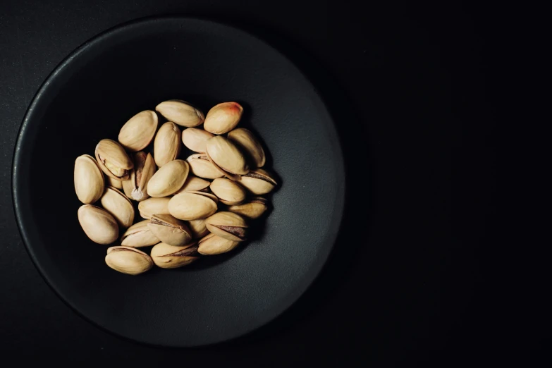 several nuts in a black bowl on a dark surface