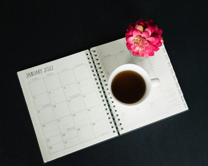 a calendar, coffee and flower on black surface